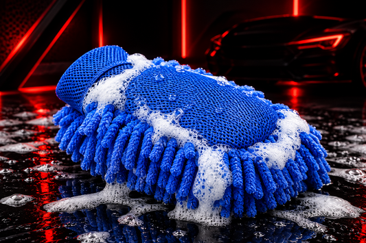Gant de lavage microfibre bleu couvert de mousse, présenté près d’une voiture

